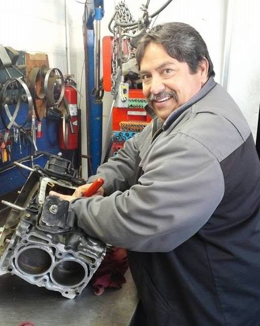 A mechanic at the workbench at Louie's Auto Repair with an engine block stripped down in front of him